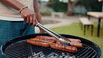 Hand, barbecue and grill sausage for party or new year celebration in backyard with food. BBQ, cooking meat and person with tongs outdoor for lunch preparation, meal and cookout event on weekend