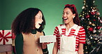 Christmas, present and women in studio, surprise and conversation on green background. Gift box, people and friends with tree, excited and wow with Xmas, shocked and giving with package, omg or smile