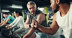 Men, cycling and fist bump with coach at gym for motivation, target or goals at fitness club. People, personal trainer and support with exercise bike, cardio workout or wellness at training center