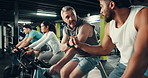 Men, bicycle and fist pump with coach at gym for motivation, target or goals at fitness club. People, personal trainer and support with exercise bike, cardio workout or wellness at training center