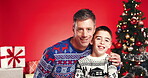 Christmas, hug and face of father and son in studio for holiday season, smile and bonding. Festive celebration, love and December break with man and child on red background for family and support