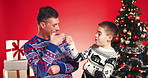 Christmas, fist bump and face of father and son in studio for holiday season, smile and bonding. Festive celebration, love and December with man and child on red background for family and support
