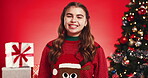 Christmas tree, face and smile of girl on red background for festive excitement or tradition. Celebration, event and season with happy child in studio for gifts or presents in December holidays