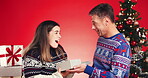 Christmas, gift and hug with couple in studio together for bonding and love for present. Wow, celebration or smile with man and woman embracing on red background for festive tradition or holidays