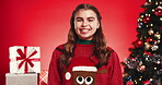 Christmas tree, face and smile of girl child on red background for festive excitement or tradition. Celebration, event and season with happy kid in studio for gifts or presents in December holidays