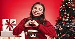 Christmas tree, heart hands and smile of girl child on red background for festive excitement or tradition. Celebration, event and face of kid in studio for gifts or presents in December holidays