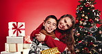 Christmas, face and kids with gift, hug and siblings for love and holiday celebration. Children, embrace and xmas with brother, sister and family portrait for vacation on red studio background