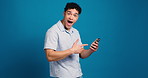 Surprised, face and man with smartphone, pointing and reaction for good news on social media or app. Blue background, excited or person with mobile for chat, mockup space and gesture for notification