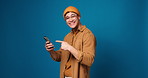 Happy man, face and pointing with phone in studio for winning or good news on a blue background. Portrait, male person or model with mobile smartphone or fist pump for advertising app on mockup space