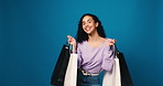 Happy woman, face and studio with shopping bags for payment or purchase on a blue background. Portrait, female person or model with smile or gifts for discount shopper, sale or deal on mockup space