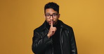 Man, face and hush in studio for secret, silence or mock up space for detective on yellow background. Person, spy and surveillance agent with sign for privacy, search and investigation in Thailand
