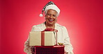 Gift, Christmas and face of old woman in studio for holiday season, retirement and smile. Festive celebration, xmas vacation and December break with elderly person on red background for present