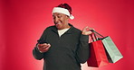 Christmas, gift and old man in studio, cellphone and happiness on red background. Xmas, smile and senior person with presents, smartphone and social media with internet, holiday season or funny meme