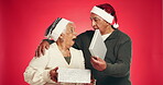 Christmas, gift and surprise with old couple in studio for love, holiday season and festive celebration. Romance, xmas present and bonding with elderly man and woman on red background for smile