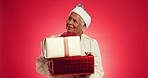 Christmas, gift and thinking with face of old woman in studio for reflection, holiday season and vacation. Festive celebration, Xmas present and vision with elderly person on red background space