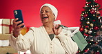 Senior, happy woman or selfie with shopping bag for christmas memory on a red studio background. Elderly, female person or laughing with picture for festive celebration, photography or capture moment