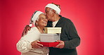 Gift box, hugging and senior couple with christmas surprise in studio for marriage tradition on holiday. Love, happy and elderly man with woman for xmas presents with celebration by red background.