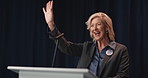 Mature woman, wave and podium for election, campaign and greeting with mic on stage for political party. Person, happy and politician with hello, smile or motivation for voter support at convention