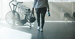 Ready, stationary bike and legs of woman in gym for exercise equipment, cardio and fitness. Walking, cycling machine and performance with back of person for wellness club, bag and start training