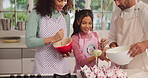 Parents, girl and help with cupcake in kitchen, skills and support with bake sale project. People, mother and daughter with father, smile and learning with muffins for small business in family house