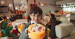 Candy, face and halloween with boy in living room of home for celebration, holiday or tradition. Bucket, costume and smile of happy child in apartment with sweet treats for trick or treating