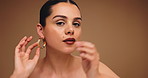 Face, woman and earrings with makeup in studio for beauty, cosmetics transformation and makeover. Portrait, female person and accessories with glamour, getting ready and self care on brown background