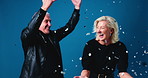 Couple, celebration and happy in studio with confetti, hug and competition giveaway on blue background. Mature man, woman and embrace with smile, lottery and excited with glitter rain with goals