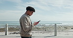 Man, walking or texting with phone at beach for online directions, holiday break or search location. Tourist, person or stroll with smartphone on promenade for navigation app, tech guide or adventure