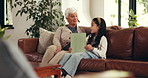 Grandmother, grandchild and reading with tablet on sofa for online learning, ebook or story in home. Grandma, granddaughter or kid with technology on couch for digital novel or education in house