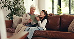 Grandma, grandchild and reading with tablet on sofa for online learning, ebook or story in home. Grandmother, granddaughter or kid with technology on couch for digital novel or education in house
