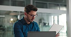 Business, man and reading document in office for accounting, finance report and company budget. Male person, laptop and paperwork for financial comparison, funding information and investment proposal