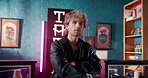 Arms crossed, face and signage with man in tattoo parlor as owner of small business or startup. Creative, ink and store with serious artist in studio shop for body art, culture or professionalism
