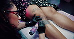 Woman, tattoo artist and client at parlor with needle, sketch or design with craft, service or job. Person, entrepreneur or small business owner with body art for legs, creativity and tools at studio