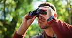 Man, sightseeing and vision with binoculars in forest for bird watching, exploration or expedition. Male person, hiker or explorer looking with scope in jungle, woods or nature for outdoor scout