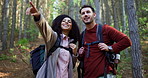 Couple, hiking and point in forest for search, landmark and happy with discussion for tourism. Man, woman and interracial relationship with smile, conversation and direction on trekking adventure