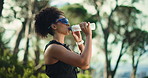 Woman, hiking and drinking water with sunglasses in forest, fitness or travel with hydration for health. Hiker, liquid electrolytes and nutrition for trekking journey, sightseeing or nature view