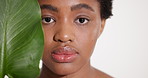 Black woman, skincare and face in studio with leaves, organic makeup and confident on white background. African girl, model and tropical plant in portrait, beauty and sustainable cosmetics in Nigeria
