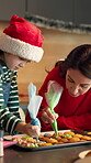 Cookies, help and Christmas with mother and daughter in kitchen for bonding, holiday season and frosting. Santa snack, support and festive dessert with woman and kid in family home for baking