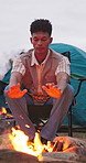 Man, relax and campfire with heat for comfort, warmth or outdoor survival in nature. Male person, camper and hands with flame, firewood or camp fire on chair for travel or cozy adventure on campsite