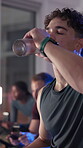 Tired, man and drinking water at spin class in gym for hydration, intense workout or sweating. Night fitness, breathing and athlete with liquid bottle for thirst, cycling recovery and exercise break