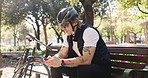 Man, cyclist and phone with bicycle on bench for break, rest or navigation app in outdoor park. Male person, user or bike with helmet on mobile smartphone for travel, commute or location in nature