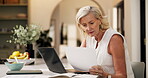 Typing, review or mature woman in home with paper, online report or editing of blog post. Reading, WFH and journalist in kitchen with tech, information and source feedback for digital article.