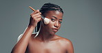 Face, brush and black woman in studio, shine and foundation on gray background. Space, makeup tool and African person with beauty, cosmetics and dermatology with glow, confidence and aesthetic