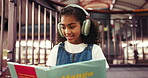 Learning, child and reading book with headphones, library and happy with fiction, knowledge or info. Girl, smile and growth with literature, education and kid with noise canceling tech in school