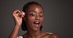 Black woman, mascara and makeup for beauty in studio for eyelash volume, lash extension and change. Smile, female person and brush and transformation, cosmetic growth and self care on dark background