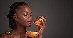 Grapefruit, skincare and smell with black woman in studio for vitamin c, beauty and natural cosmetics. Exfoliating enzyme, facial glow and dermatology with person and fruit on dark background