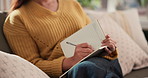 Woman, hands and writing with book for diary reminder, checklist or agenda on sofa in home. Female person, planner or writer with notebook, pen or notes for daily schedule, tasks or planning activity