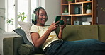 Coffee, headphones and phone with black woman on sofa in home living room for beverage break. App, scroll and music with happy person in apartment for internet search and cup of tea with laugh