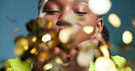 Blowing, glitter and smile of black woman in studio for celebration, event or milestone. Confetti, gold and success with excited African person on blue background for achievement or announcement
