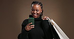 Phone, shopping bag and funny black woman in studio with discount deal, promotion or fashion. Mobile, shopper and person laugh with gifts, social media review and bargain on brown background space